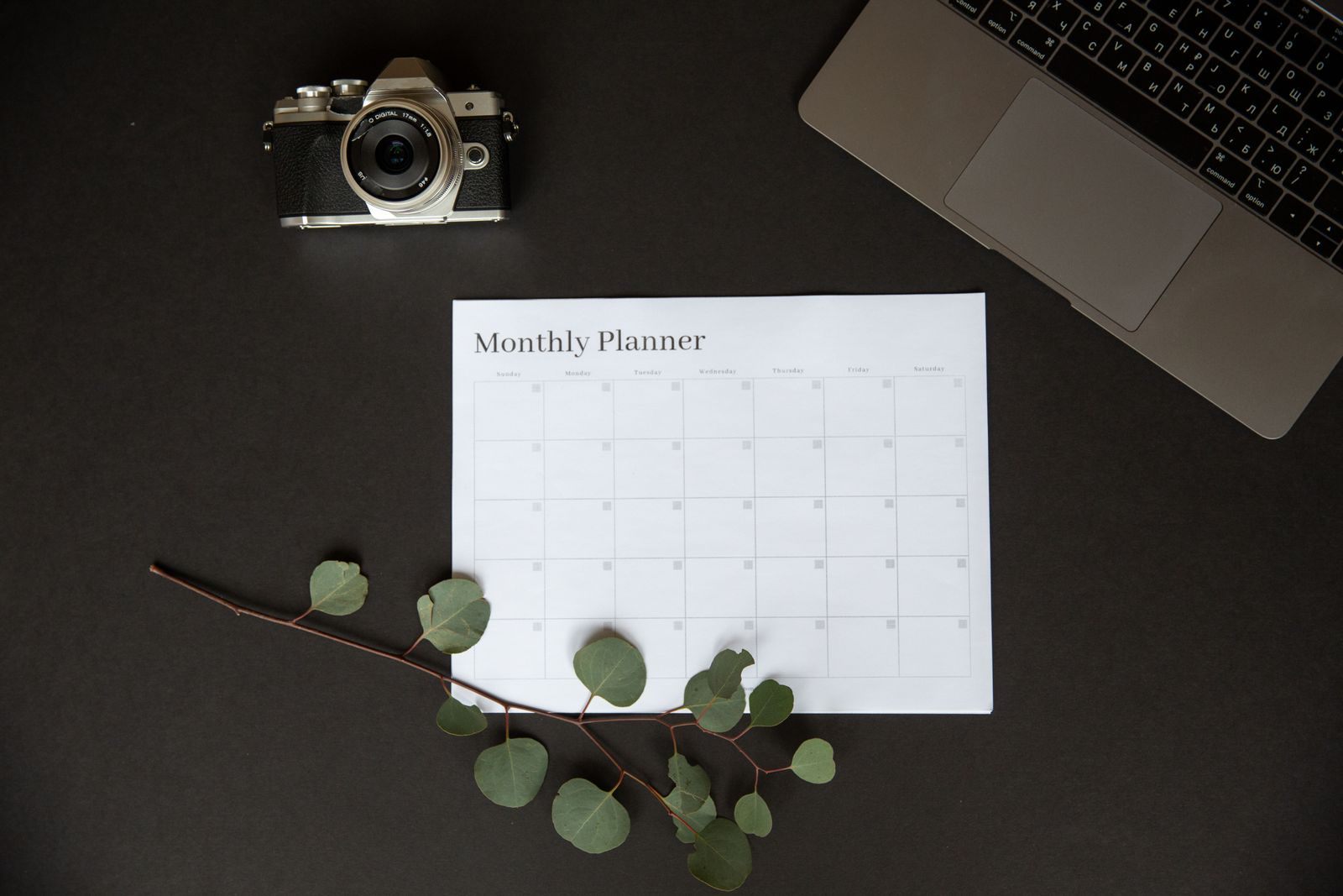 Monthly planner, laptop and camera laid out for trip planning